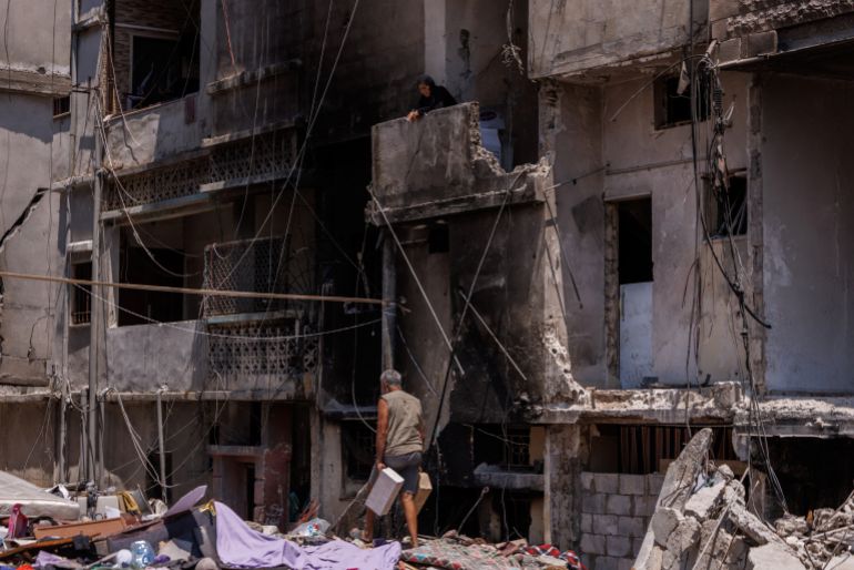 A woman smokes a cigarette as she stands on the balcony of a building damaged in an Israeli airstrike, while Hassan Hejazieh carries bricks as he walks amid the rubble, attempting to rebuild his home after returning home following displacement during the war, following the Israel-Lebanon deal, in Tyre, southern Lebanon, July 5, 2026. REUTERS/Zohra Bensemra