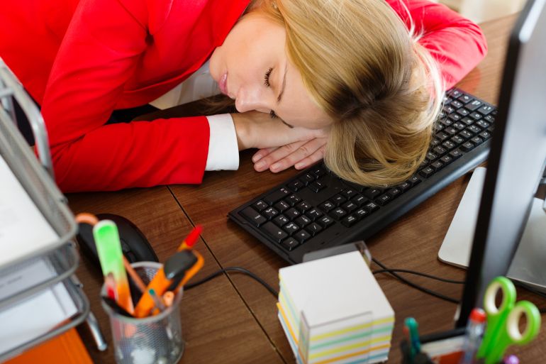 shutterstock_247276501-1776946644 Young businesswoman in red sleeping at office desk