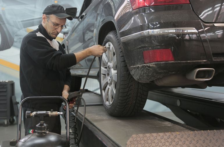 syyyart-1785409562 A male mechanic checks tire pressure on a vehicle in a workshop setting, showcasing automotive expertise.