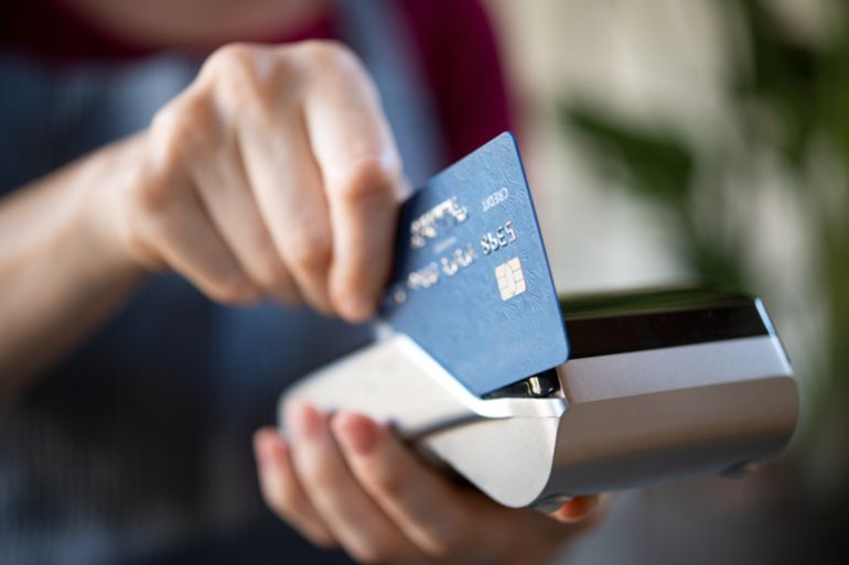 1atm-1783336278 Close up hands of waitress holding credit card machine terminal and swiping debit card to pay the bill. Payment with a credit card through terminal at restaurant or cafeteria. adobe stock