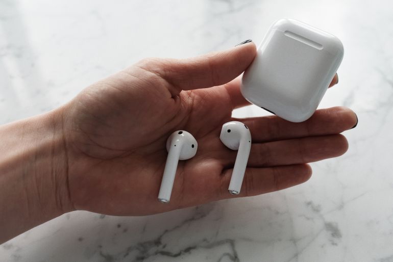 21805-1-1786458309 A woman's hand holding wireless earbuds and a charging case on a marble surface.