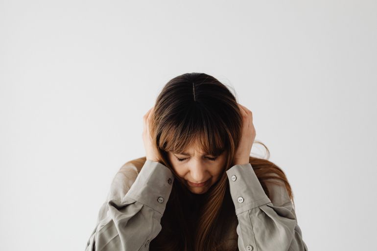 3375-1787506088 Woman with closed eyes holding head, conveying stress and emotions against a plain white background.