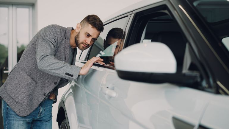 36729880-1786573548 Man carefully examining a modern white car at a dealership showroom.