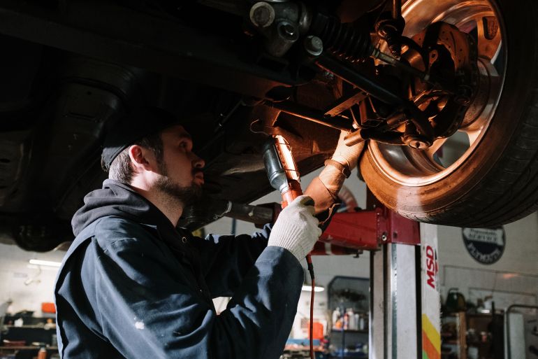 4489749-1786574323 Mechanic examining car's undercarriage at a garage, focusing on vehicle maintenance.