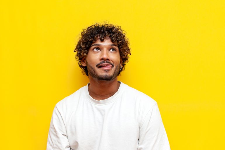 456754-1786637988 young curly indian man licking his lips and imagining on a yellow isolated background, a curious guy is dreaming and thinking looking up and showing his ... See More by Богдан Маліцький @ادوبي ستوك