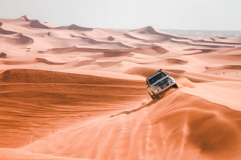 4968848-1786794175 A sports utility vehicle embarks on a thrilling desert safari, navigating vast sand dunes under bright daylight.
