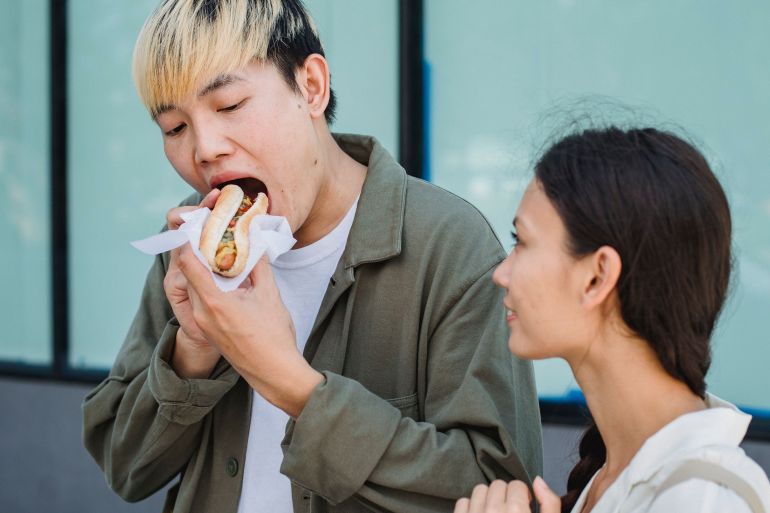5225480-1787667596 Asian couple sharing a moment while enjoying a delicious street food snack outdoors.