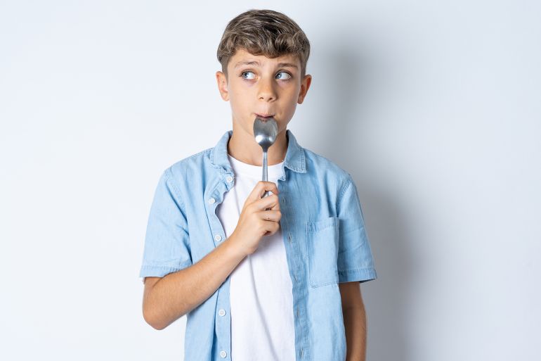 568-1786637984 Very hungry Beautiful kid boy wearing casual clothes holding spoon into mouth dream of tasty meal by Roquillo @ادوبي ستوك