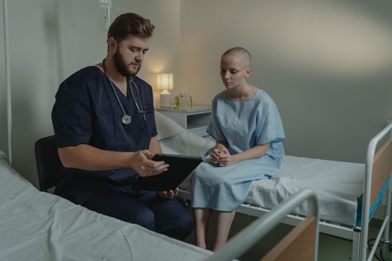 6010865-1787326667 A doctor in a hospital ward consulting a patient with a digital tablet.