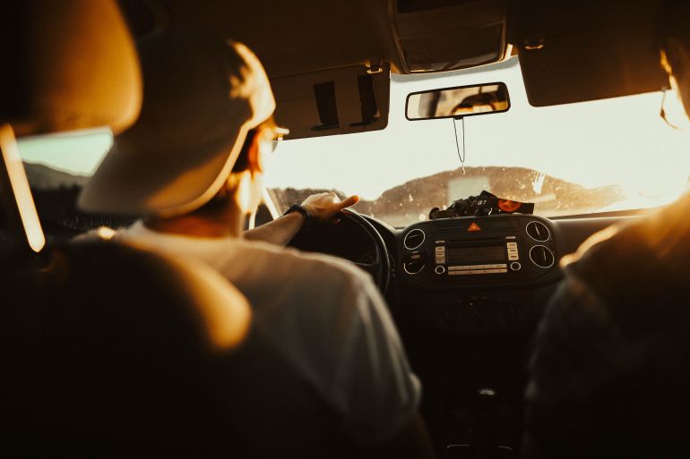 620335-1786957537 Man driving car with passenger at sunset, capturing warm sunlit atmosphere.