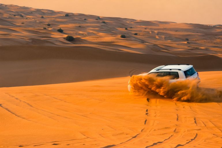 67753-2417260-1786792697 A thrilling SUV driving through the sand dunes of Dubai's desert landscape at sunset.