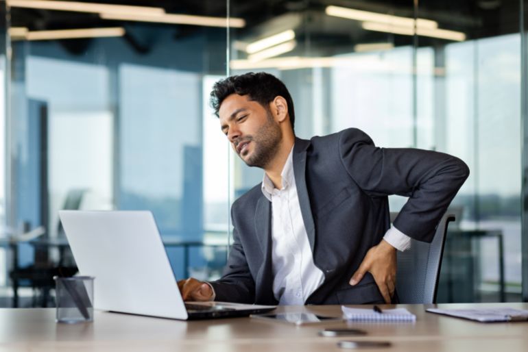 adobestock_676561166-1787664646 Back pain, businessman working long time sitting at laptop inside office, man massaging back muscle, pain and fatigue, worker in business suit at workplace. المصدر: أدوبي ستوك