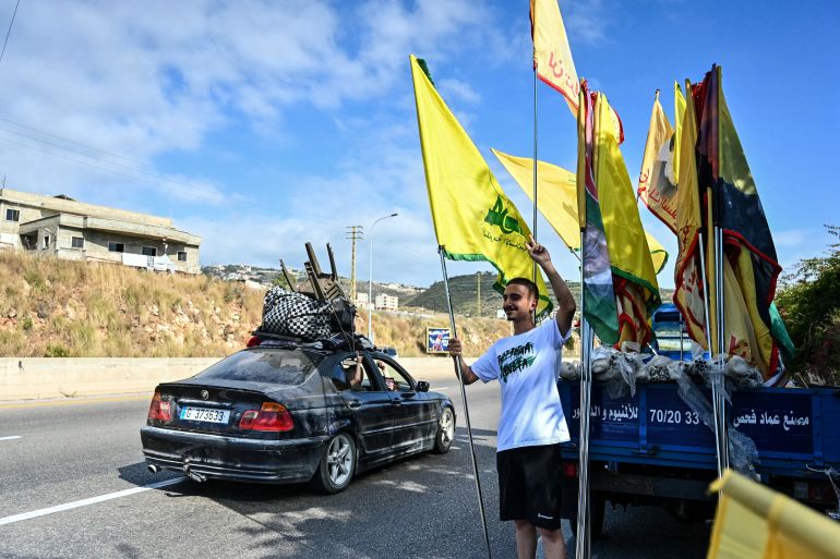 afp_6a34414b5455-1781809483 Displaced families drive past a man holding the Shia-Muslim Hezbollah party flag as they drive along the highway through the area of Jiyeh as they return to their home villages in southern Lebanon on June 15, 2026.