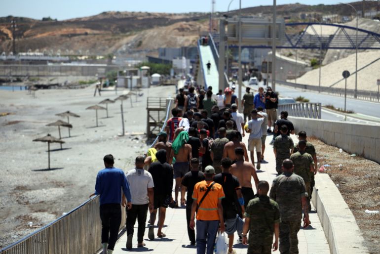 TOPSHOT - A group of migrants approach the border post to make their way back to Morocco, escorted by Spanish infantry soldiers, in the Spain's north African enclave of Ceuta, on August 2, 2026.