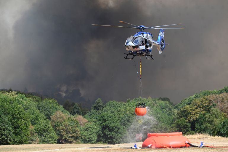afp_6a7f1bf4dea5-1786715124 A police helicopter loads water to fight a forest fire in Huertgenwald, western Germany on August 14, 2026.