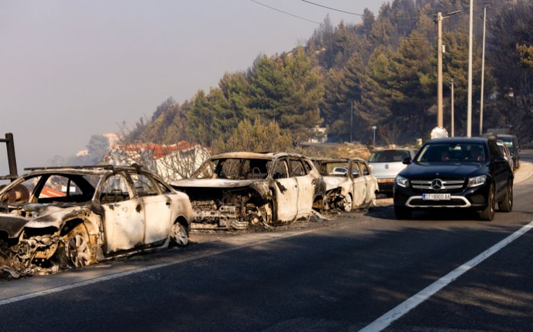afp_6a7f1cab2759-1786715307 A car drives past burnt cars on a road after a wildfire near the town Omis, some 30 kilometres south of Split, on August 14, 2026.