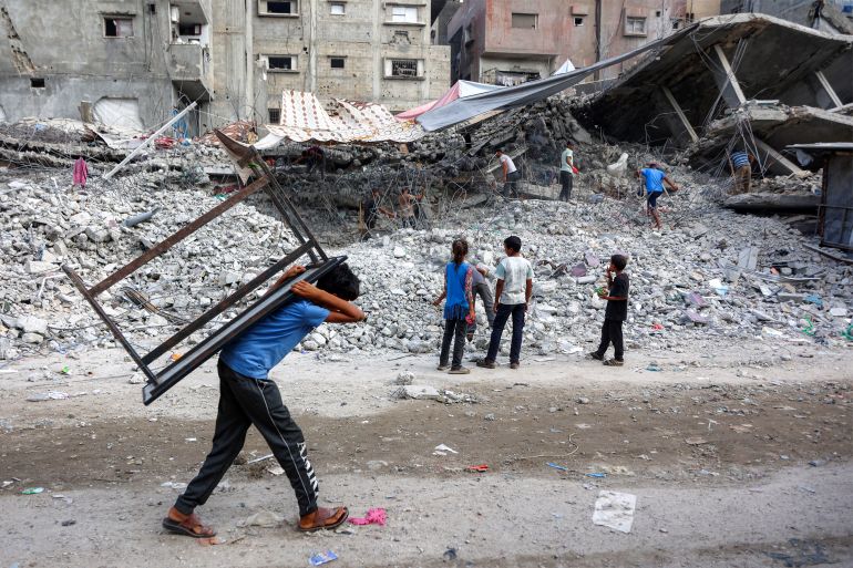 A boy walks carrying a table on his back past salvage workers scrapping the rubble of a building that was destroyed during Israel's war against Hamas in Gaza, to use the recycled remains in the future, in Gaza City on August 16, 2026.