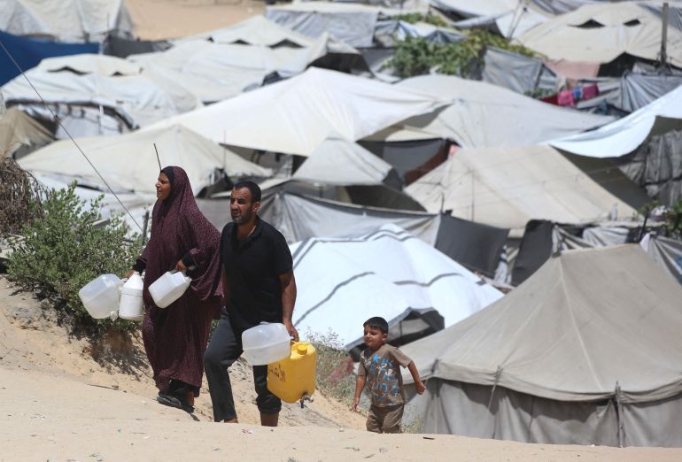 Internally displaced Palestinians carry walter containers past hundreds tents now housing them after their homes were destroyed by the Israeli military, in Khan Yunis southern Gaza Strip on August 11, 2026.