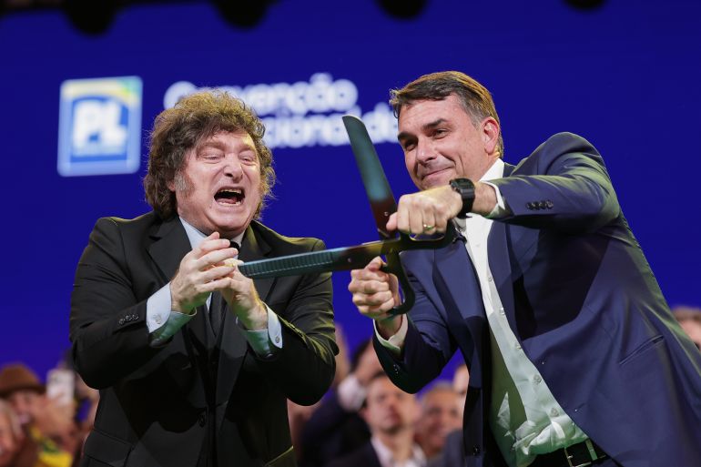 Brazilian Sen. Flavio Bolsonaro, right, handles an oversized pair of scissors, accompanied by Argentina's President Javier Milei during the Liberal Party convention where Bolsonaro was confirmed as the party's presidential candidate, in Sao Paulo, Saturday, July 25, 2026. (AP Photo/Ettore Chiereguini)