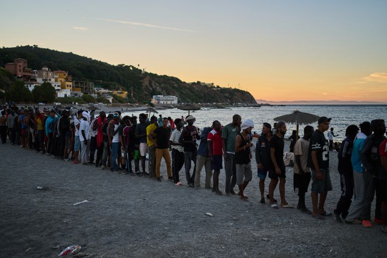 ap_6a718e3957b98-1785826873-1 Migrants who crossed from Morocco into Spain line up for food distribution on a beach in the Spanish enclave of Ceuta, Monday, Aug. 3, 2026. (AP Photo/Bernat Armangue)