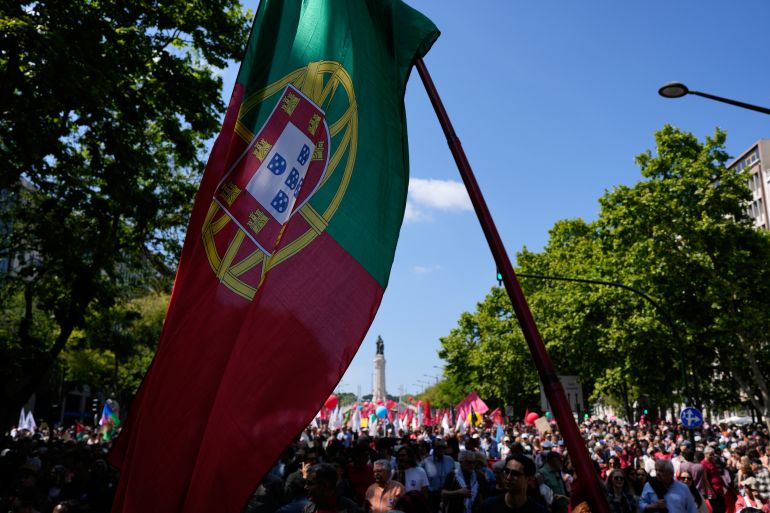 ap_6a85f9050777b-1787164933 A Portuguese flag is carried among tens of thousands marching down Lisbon's Liberdade Avenue, Saturday, April 25, 2026, celebrating the anniversary of the April 25 1974 Carnations Revolution that restored democracy in Portugal. (AP Photo/Armando Franca)