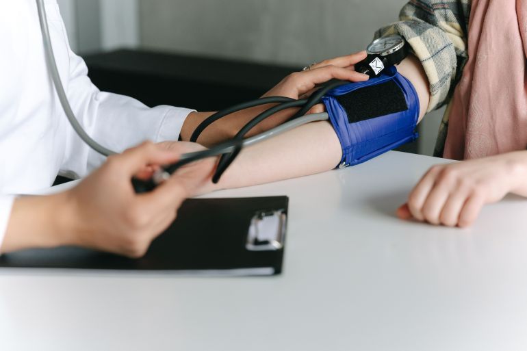 dm-1785499942 A healthcare worker uses a sphygmomanometer to check a patient's blood pressure in a medical office.