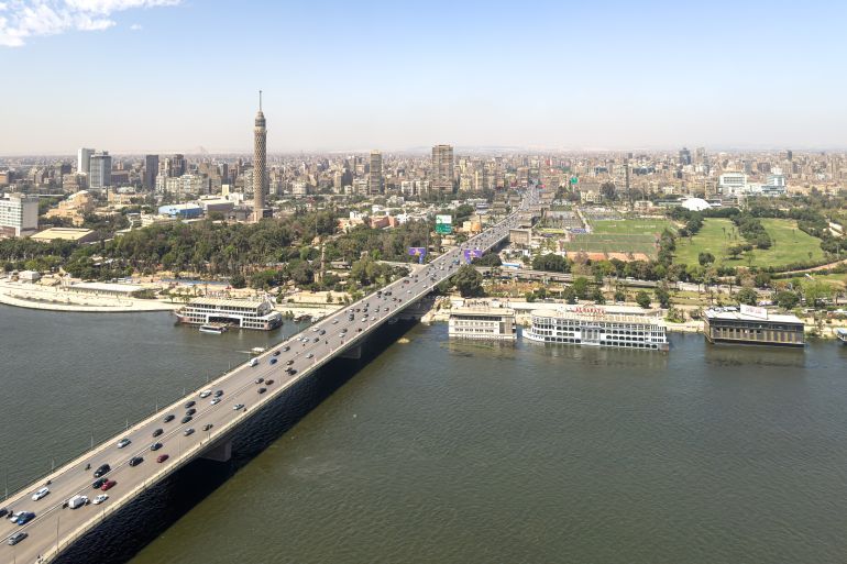 f-2164417-1787870197 This captivating aerial image showcases the vibrant heart of Cairo, Egypt, with the Nile River flowing beneath a bustling bridge connecting both riverbanks. The iconic Cairo Tower rises prominently from the verdant landscape of Zamalek Island, offering panoramic views of the sprawling metropolis. Lush parks, modern buildings, and historic urban sprawl unfold in the distance, capturing the dynamic blend of culture, history, and modernity. Ideal for travel, cultural, or editorial use, this image reflects Cairo’s strategic location, architectural landmarks, and the life-giving presence of the Nile at the city's core.