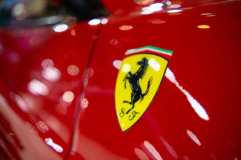 Detailed view of a classic sports car emblem on sleek red paint, showcasing luxury and style.