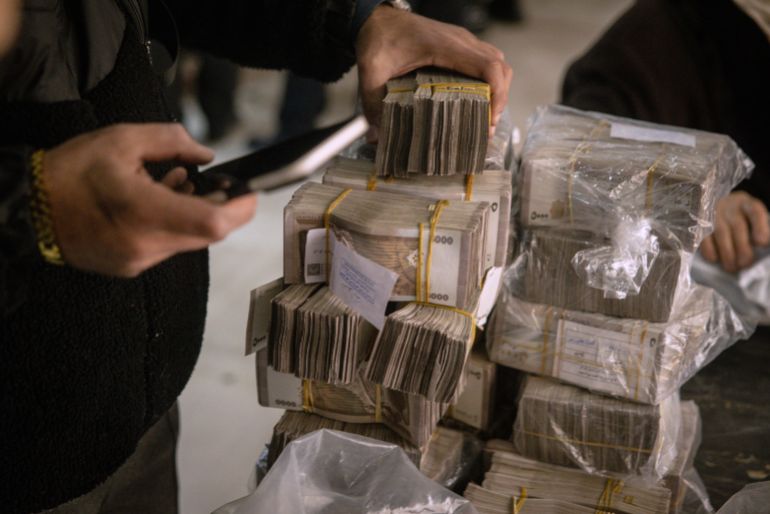 getty_68133e98f0-1746091673 DAMASCUS, SYRIA - DECEMBER 24: A man counts stacks of Syrian pounds after exchanging U.S dollars at the Central Bank Of Syria on December 24, 2024 in Damascus, Syria. On December 8, rebel forces in Syria retook the capital and several other cities from longtime ruler Bashar al-Assad, who fled the country for Moscow. The fall of the Assad regime marks a new chapter for Syria, which has been mired in a multi-party civil war since 2011, sparked by the Arab Spring uprisings. (Photo by Chris McGrath/Getty Images)