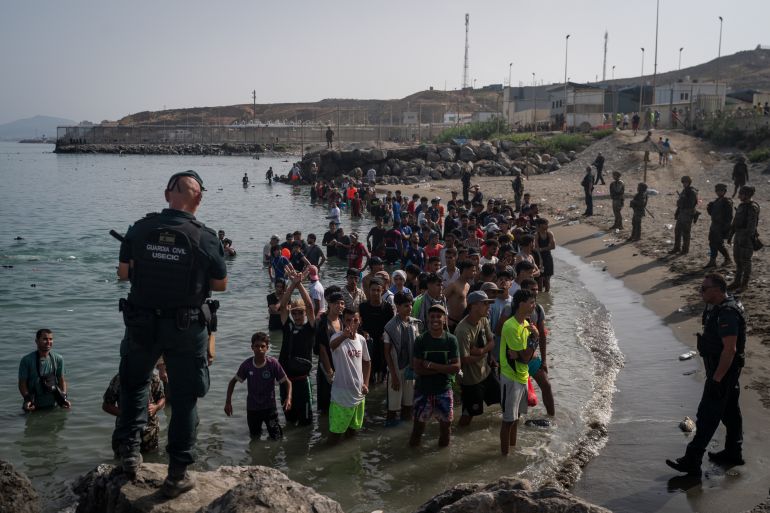 getty_6a6dd4fe51-1785582846 CEUTA, SPAIN - JULY 31: Members of the Guardia Civil USECIC guard migrants on Tarajal beach after crossing the border between Spain and Morocco on July 31, 2026 in Ceuta, Spain. Spain's interior ministry has said it's deploying 60 members of the armed forces and an additional 30 Guardia Civil officers to Ceuta after tens of thousands of migrants entered the Spanish enclave in North Africa on Thursday. A large number of people swam through the Tarajal breakwater to enter the Spanish territory from neighboring Morocco, while others scaled the border fence. Some estimates have said that around 49,000 migrants made the crossing, with the surge of arrivals overwhelming migrant reception centres, with many sleeping on the streets overnight. (Photo by Adri Salido/Getty Images)