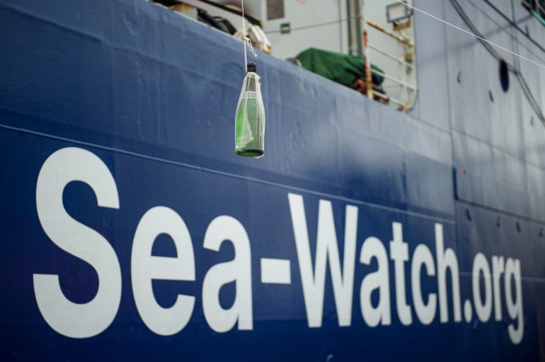 getty_6a7a05a1dc-1786381729 HAMBURG, GERMANY - NOVEMBER 03: A bottle of sparkling wine is hanging in front of the hull of the Sea-Watch 5 rescue ship during its first presentation to the public and official baptism on November 3, 2022 in Hamburg, Germany. Sea-Watch 5 is the latest ship of Berlin-based rescue initiative Sea-Watch e.V. that will go into operation in the Mediterranean Sea to rescue refugees in distress while crossing by boat from northern Africa. (Photo by Gregor Fischer/Getty Images)
