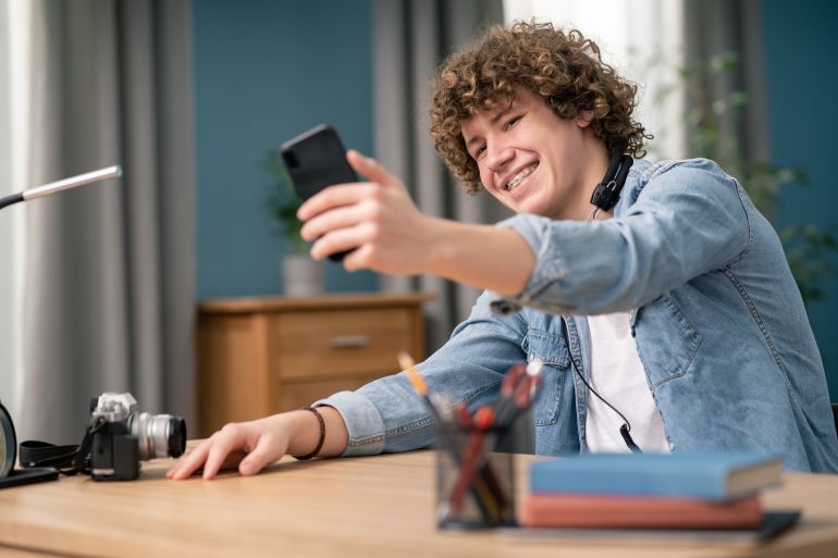 gettyimages-1308400603-1786277486 Teenager male use smartphone records video for social networks makes funny faces, flirts laughs looking carefree, dances grimaces in front of camera, having fun