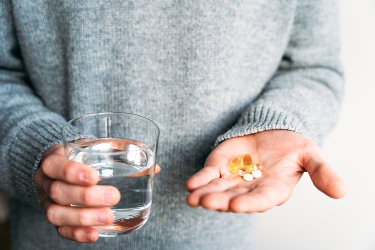 gettyimages-2255650221-1784227879 Person holding water and dietary supplements, illustrating a balanced approach to health, hydration and daily self-care in a clean, minimal environment