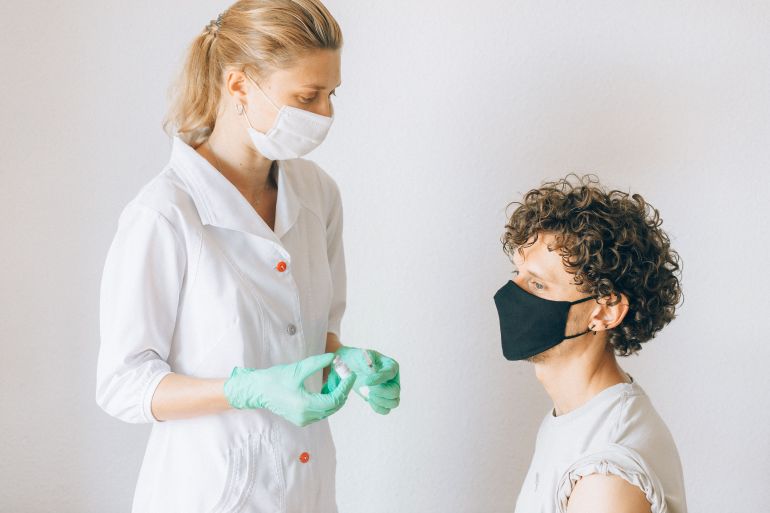 jjj-1786115268 A nurse wearing a mask prepares a vaccine for a masked patient indoors, promoting health care.