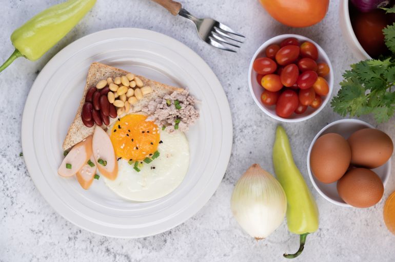 pe-1-1785527758 Breakfast consists of fried eggs, sausage, minced pork, bread, red beans and soy on a white plate. المصدر: ماجنيفِك