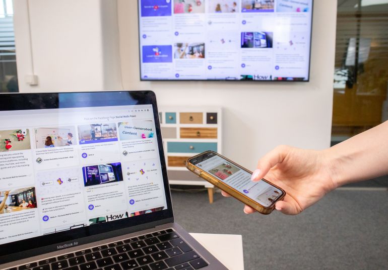 Person using smartphone and laptop in a modern office environment with digital screens.