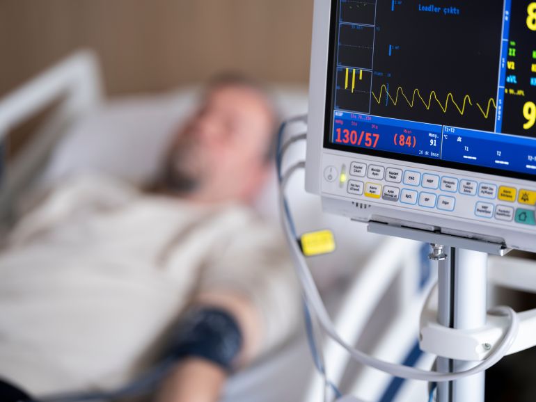 qlb-1785500509 Patient in hospital bed with heart monitor showing blood pressure and heart rate.