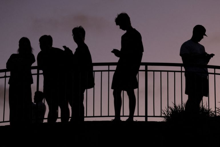 reuters_69393f31-1765359409 People use their mobile phones, ahead of new law banning social media for users under 16 in Australia, at dusk in Brisbane, Australia, December 8, 2025. REUTERS/Hollie Adams