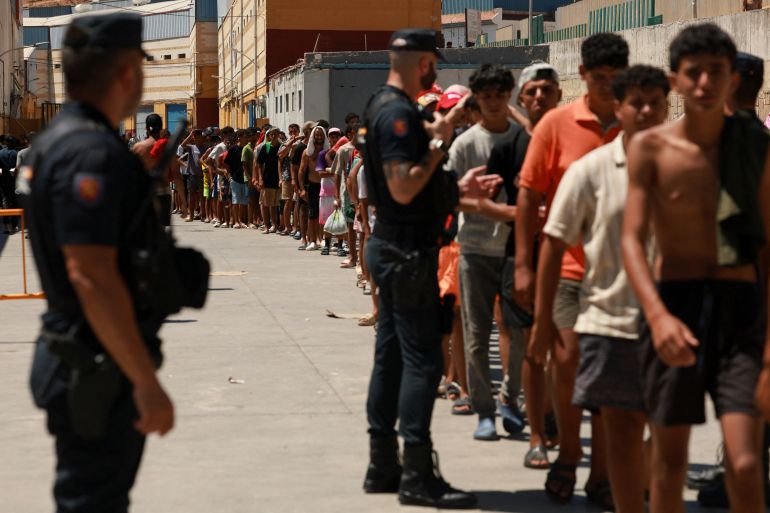 Migrants queue to receive food staples from local NGO Media Luna Blanca in an industrial area where they are sleeping amid recent mass crossings by migrants on foot and by sea from Morocco into the Spanish territory, in Ceuta, Spain, August 6, 2026. REUTERS/Violeta Santos Moura
