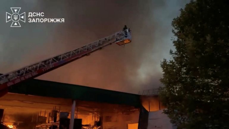 reuters_6a7ccbab-1786563499 Emergency personnel works to extinguish fire at a hardware store following, what the regional governor said was, in the aftermath of a Russian drone attack in Zaporizhzhia, Ukraine, August 12, 2026 in this screengrab taken from a handout video. STATE EMERGENCY SERVICE OF UKRAINE IN ZAPORIZHZHIA REGION/Handout via REUTERS THIS IMAGE HAS BEEN SUPPLIED BY A THIRD PARTY. MANDATORY CREDIT. OVERLAY FROM SOURCE. VERIFICATION: -Business signs, utility poles and buildings, and parking lot layout matched archive and satellite imagery -Date confirmed by statement from the regional governor who said that a Russian attack caused a fire at a shopping mall in Zaporizhzhia -NASA FIRMS detected thermal activity at the location on August 12 -No older versions found posted online before August 12