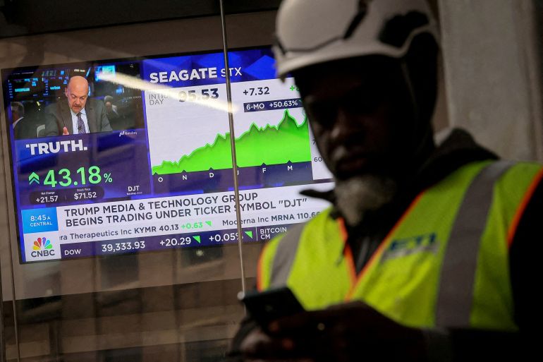 FILE PHOTO: A man looks at this phone as a screen displays trading information about shares of Truth Social and Trump Media & Technology Group, outside the Nasdaq Market site in New York City, U.S., March 26, 2024. REUTERS/Brendan McDermid/File Photo