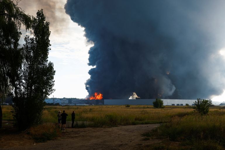 People watch as smoke rises over a warehouse, which was hit by a Russian drone strike, amid Russia's attack on Ukraine, in Kyiv region, Ukraine, August 27, 2026. REUTERS/Valentyn Ogirenko