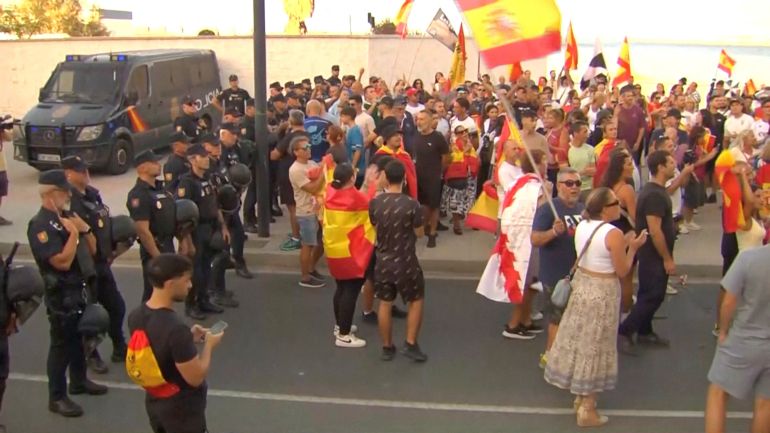 reuters_6a91ca45-1787939397 Law enforcement personnel watch while protesters hold Spanish flags, as Ceuta residents destroy migrant camp by the beach, in Ceuta, Spain, August 27, 2026, in this screen grab taken from a handout video. FORTA/Handout via REUTERS THIS IMAGE HAS BEEN SUPPLIED BY A THIRD PARTY. SPAIN OUT. NO COMMERCIAL OR EDITORIAL SALES IN SPAIN