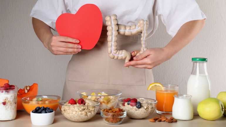 shutterstock_2131991277 غلاف فيديو: نمط الحياة الصحي يقلل خطر التهاب الأمعاء Woman holding paper heart and large intestine model near table with food, closeup. Balanced nutrition for healthy digestive system shutterstock_2131991277