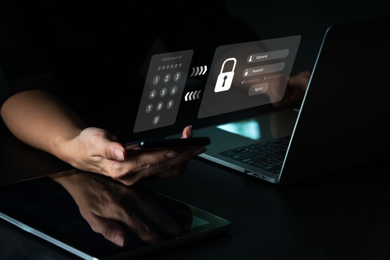 shutterstock_2152929947-1779875366 A woman with a mobile phone and a laptop computer has a safe account. Hacking a Phishing mobile phone with a password to get access to a smartphone, internet security issues.