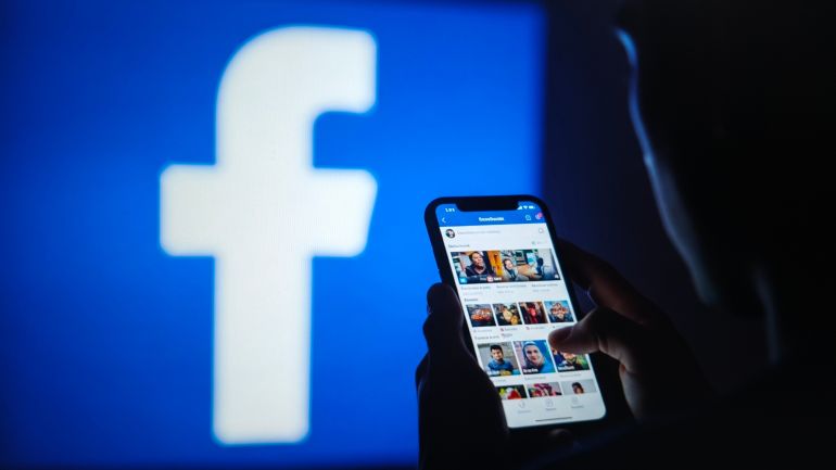 Closeup of a person using a smartphone with facebook feed, large facebook logo in background, New York City, 23 October 2025