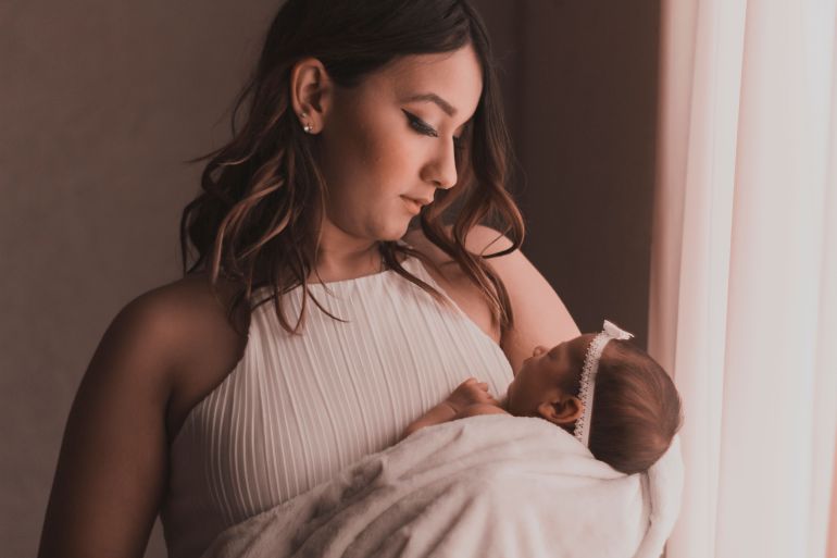 3398405-1790677209 A mother lovingly cradles her baby by a window, capturing a tender moment.