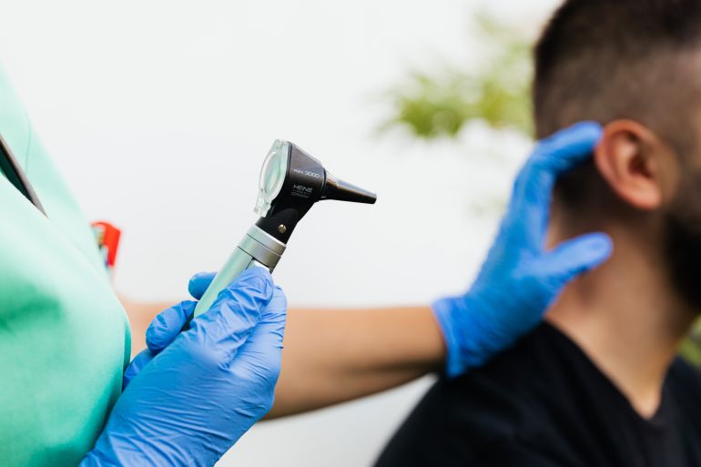 5206950-1787319958 Healthcare professional examining patient's ear with an otoscope in a clinical setting.