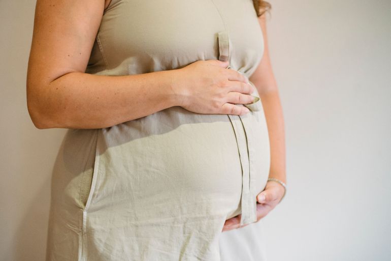 5424708-1790677392 Close-up of a pregnant woman gently cradling her belly, showcasing maternal affection and anticipation.