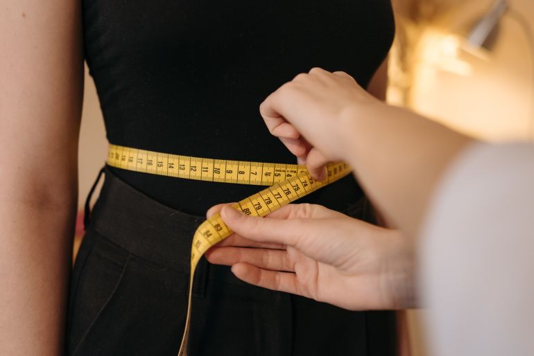 Close-up of tailor's hands measuring a person's waist with a yellow tape.